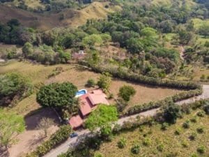 Aerial view of a hacienda with stables, horse corral, and lush green landscape in Dominical.