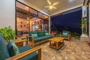 Covered outdoor living space with ocean view, ceiling fan, and garden.
