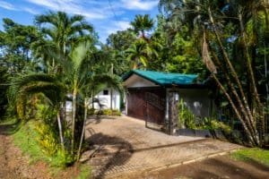 Tropical home entrance in Dominical with lush greenery and gated driveway.