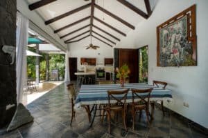 Interior of a Bali style home with high ceilings, dining table, and open kitchen.