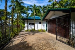 View of a Bali-style home with gated entrance and lush tropical trees.