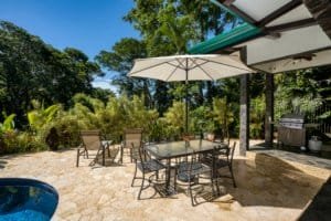 Outdoor patio with dining table, chairs, umbrella, and lush tropical garden in Dominical.