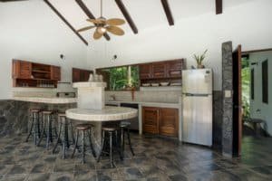 Modern kitchen in Costa Rica with wooden cabinets, stone accents, and stainless steel refrigerator.