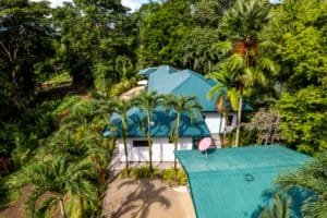 Aerial view of a Bali-style home with blue roof in lush tropical setting.