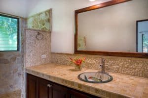 Bathroom with stone wall, wooden framed mirror, and tropical decor in Costa Rica.