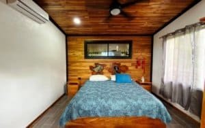 Bedroom with wooden ceiling, mountain view window, and blue bedding.