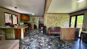 Interior view of a stone-walled living area with kitchen, seating, and large windows in Costa Rica.
