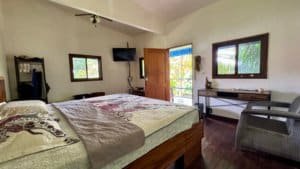 Cozy bedroom with two beds, a desk, and a doorway to a balcony in a tropical Costa Rica home.