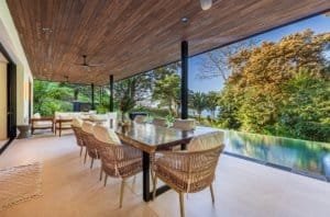 Outdoor dining area with a long wooden table on a covered patio and lush garden view.