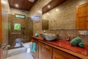 Bathroom with stone sink, rustic wooden vanity, and pebble shower in Costa Rica home.
