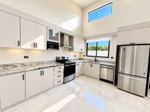 Bright kitchen with white cabinets, granite countertops, and large window overlooking outdoors.