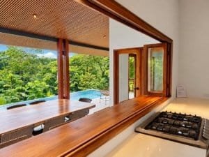 Dominical real estate: covered terrace, wood accents, open kitchen window with pool and lush jungle.