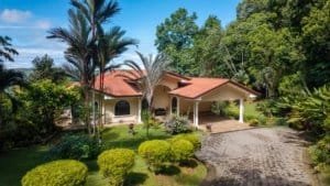 Costa Rica luxury home with ocean and mountain views, lush garden, and driveway.
