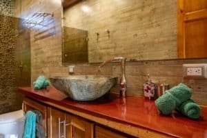 Stone vessel sink on wooden countertop in bathroom with towels and modern fixtures.