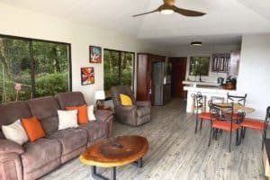 Spacious living area in Dominical home with sofa, colorful cushions and kitchen nearby.