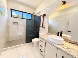 Bright ensuite bathroom with glass shower, double sink vanity and large window.