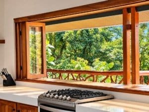 Open wooden-framed window overlooking lush tropical greenery and balcony seating.