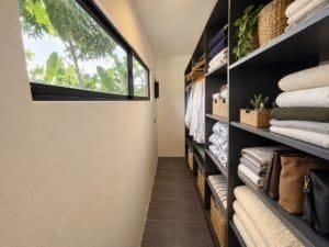 Interior view of a closet with shelves of towels and bags near a window.