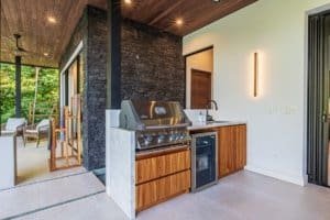 Luxury outdoor kitchenette with grill and wooden cabinetry near covered patio.