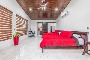 Bright master bedroom with red bedding, wood ceiling, white walls, and large windows in Costa Rica.