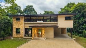 Luxury jungle home with stone accents, two-story design, covered entry, and natural surroundings.