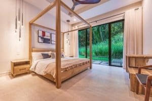 Luxurious master bedroom with a wooden four-poster bed and a view of lush greenery through sliding玻璃.