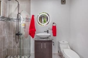 Modern bathroom with glass shower, pedestal sink, circular mirror, and red towels.