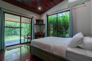 Bedroom with large sliding glass doors to lush garden and wooden ceiling.