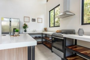 Creekside kitchen with stainless steel stove, white countertops, wooden open shelves and large side.