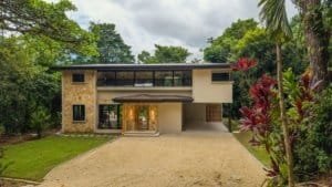 Dominical real estate: modern two-story home with stone accents, driveway, and lush tropical garden.