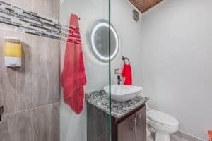 Modern bathroom with vanity, red towels, and circular mirror in Costa Rica listing.