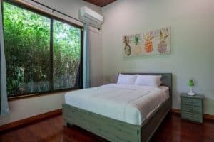 Bedroom with large window overlooking greenery, queen bed, and tropical decor.