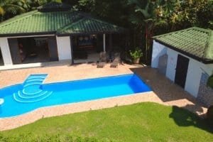 Panoramic tropical pool area with adjacent bungalow and green lawn.