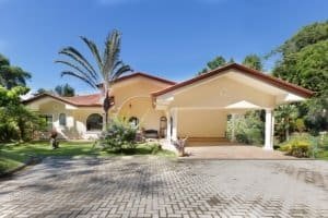 Elegant Costa Rican home with lush garden and driveway in a gated community.