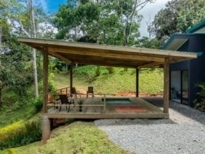 Creekside wooden patio with seating under a covered deck in tropical forest.