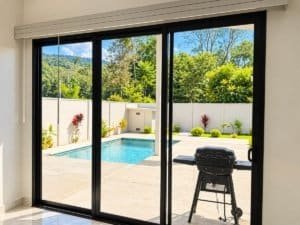 Sliding glass doors open to a backyard with a rectangular pool and lush greenery.