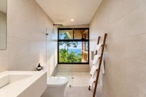 Modern bathroom with view of tropical landscape and sea through large window.