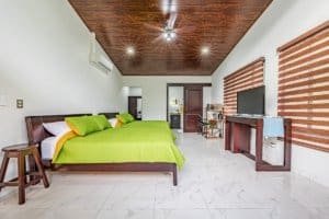 Bright master bedroom with green bedspreads, wooden ceiling, and modern desk area in Dominical Costa.