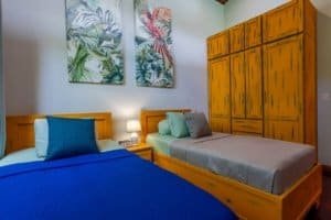 Twin-bed coastal bedroom with wooden furniture and tropical wall art.
