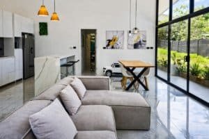 Bright modern living room with gray sectional sofa, marble flooring, large glass doors, and a dining.