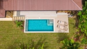 Aerial view of a rectangular blue pool with steps, sun loungers, and tropical landscaping.