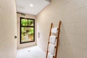 Bright tiled bathroom with a wooden towel ladder and window overlooking greenery.