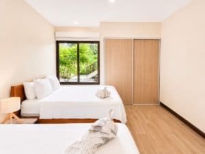 Bright bedroom with garden view, white bedding, and wooden closet doors.