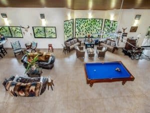 Bright living room with pool table, tropical decor, and large windows showing greenery.