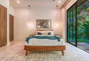 Bright bedroom with wood bed, pendant lights and sliding glass doors to greenery.
