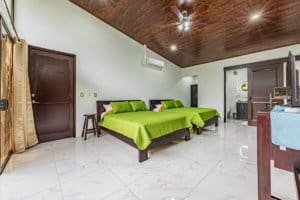 Three green-blanketed bedrooms in bright retreat with dark wood ceiling and tiled floor.