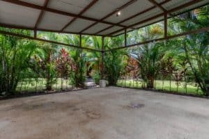 Covered patio overlooking lush tropical garden with palm trees.