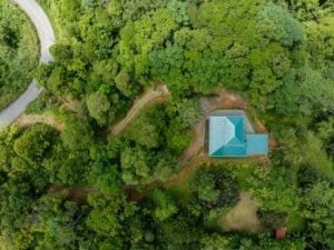 Aerial view of a blue-roofed house nestled among dense green trees and winding roads in Dominical, T.