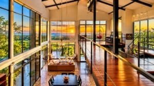 Panoramic living room with large windows, sunset ocean view, wooden flooring and modern decor.