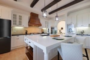 Modern kitchen with white cabinets, island, and wooden ceiling beams in Dominical.